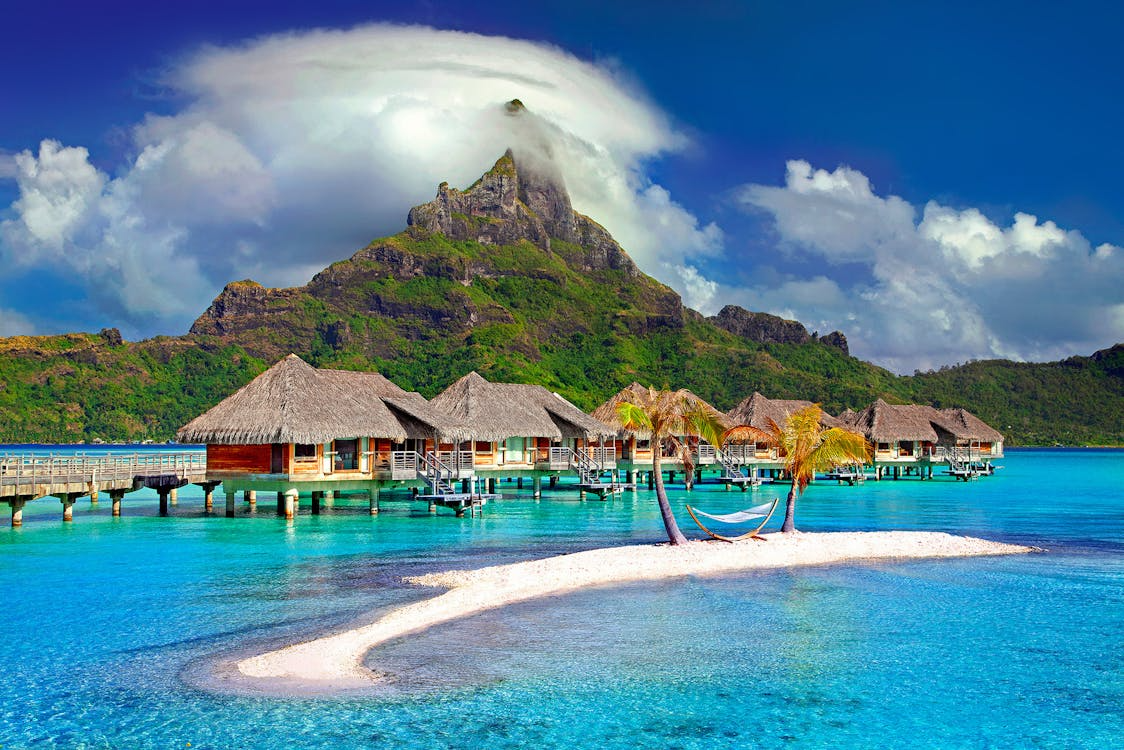 Overwater bungalows with thatched roofs on a private beach in the foreground.