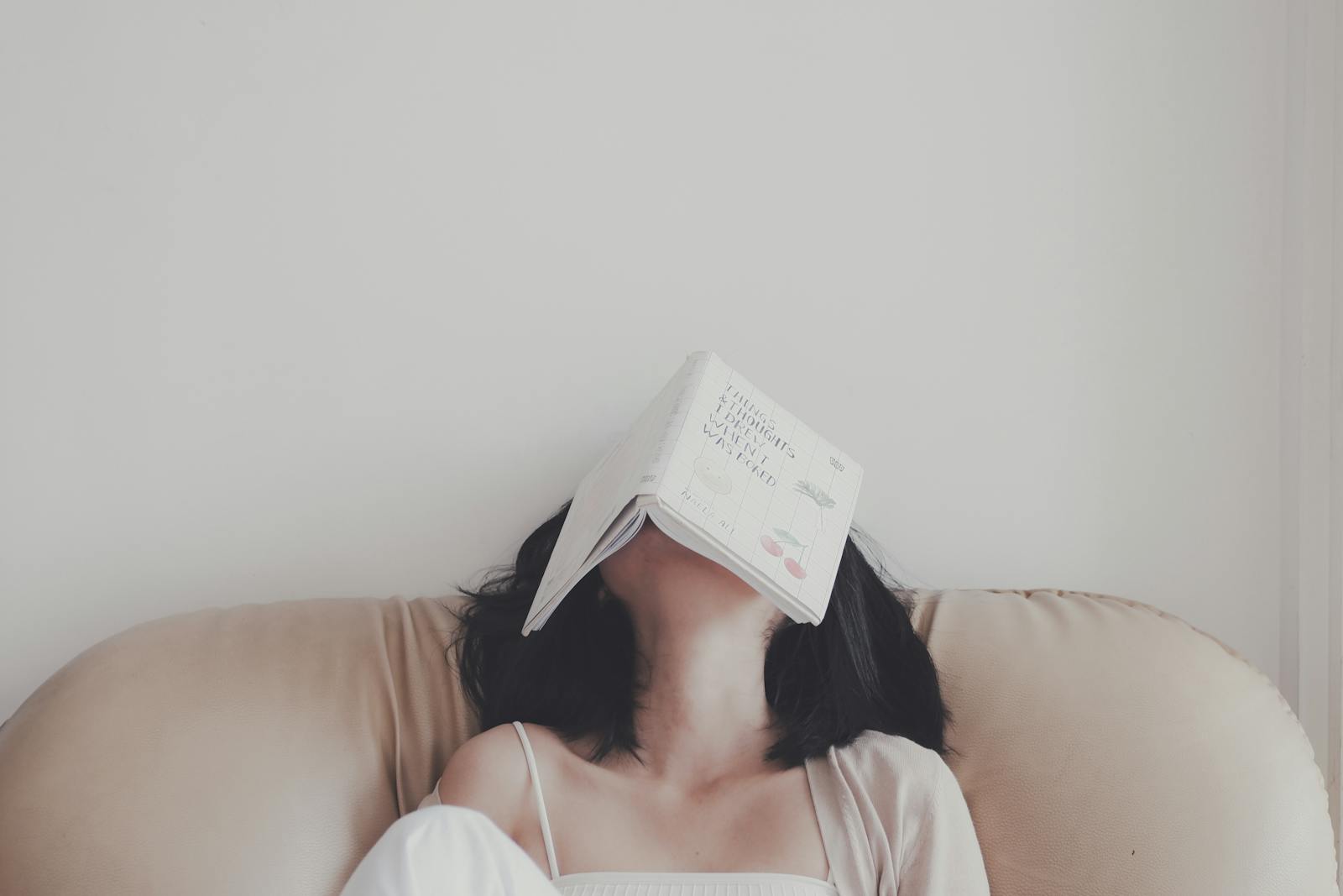 A woman relaxes indoors with an open book resting on her face, enjoying a tranquil moment.