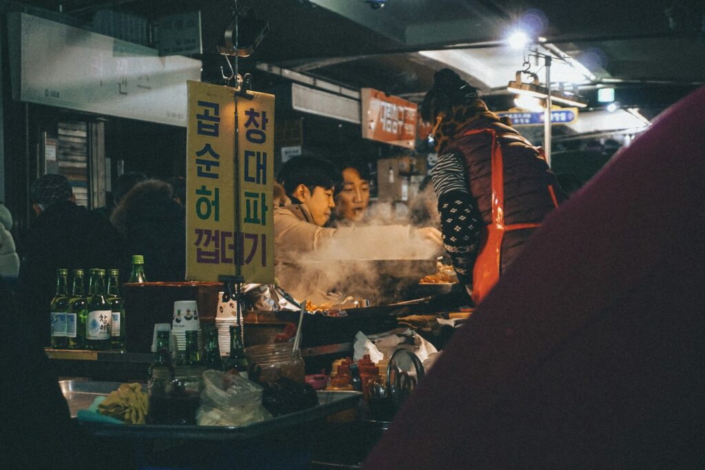 man in red and black jacket standing in front of food stall